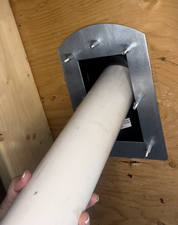 Person holding a white cylindrical object against a metal bracket on a wooden surface